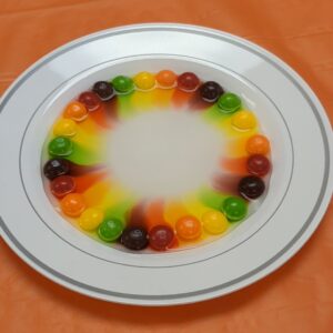 A plate of colorful candy. Water has been added, and the color is moving towards the center of the plate.
